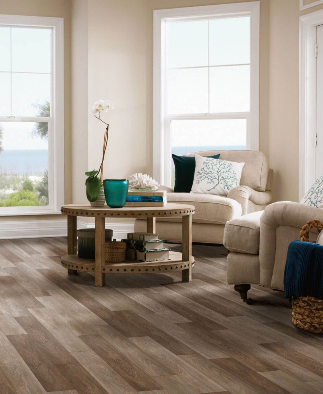 Living room with large windows, beige sofa, round wooden coffee table, and wood-look vinyl plank flooring